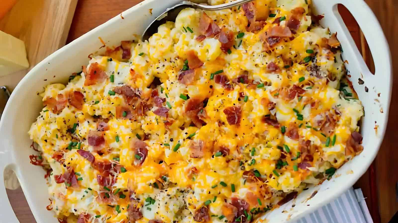 Baked potato casserole topped with melted cheese, chopped bacon, and chives in a white dish.