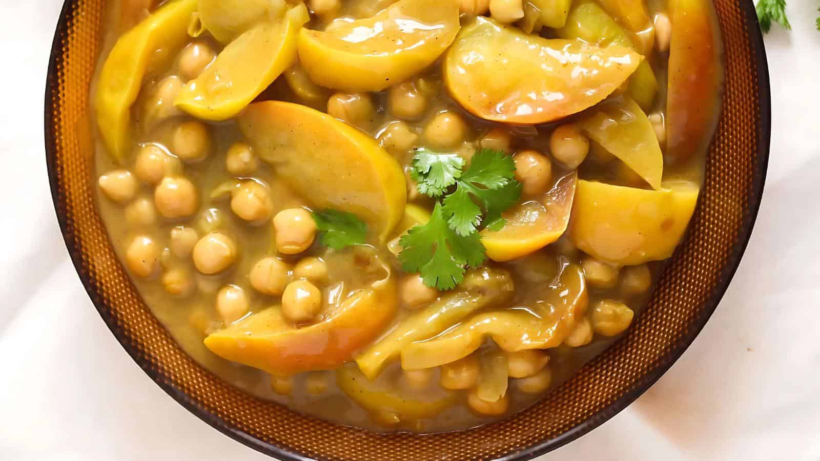 A bowl of chickpea curry with sliced apples and garnished with fresh cilantro.