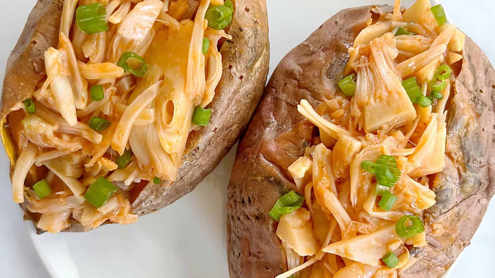 Two baked potatoes topped with shredded jackfruit and chopped green onions on a white plate.