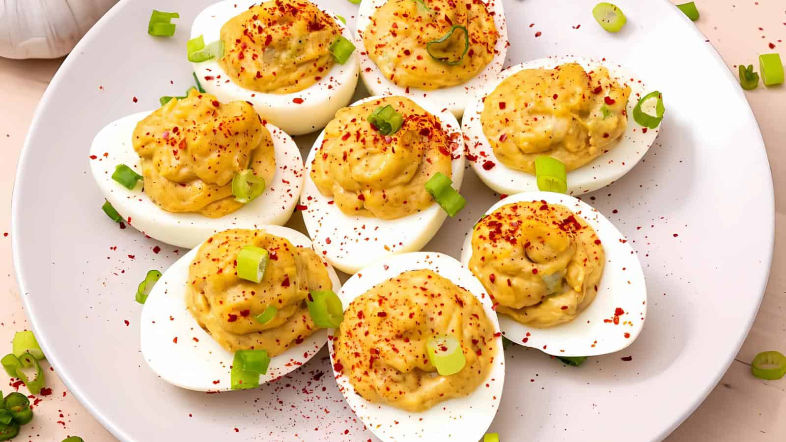 A plate of deviled eggs garnished with chopped green onions and a sprinkle of red paprika.