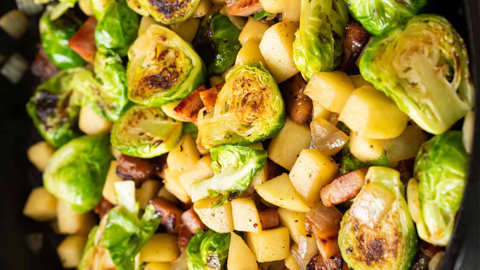 Close-up of a dish with roasted Brussels sprouts, diced potatoes, and pieces of cooked bacon.