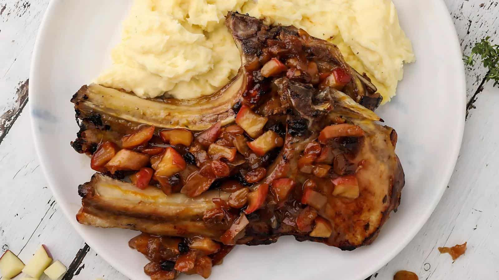 Grilled pork chop topped with diced apples, served with a side of mashed potatoes on a white plate.