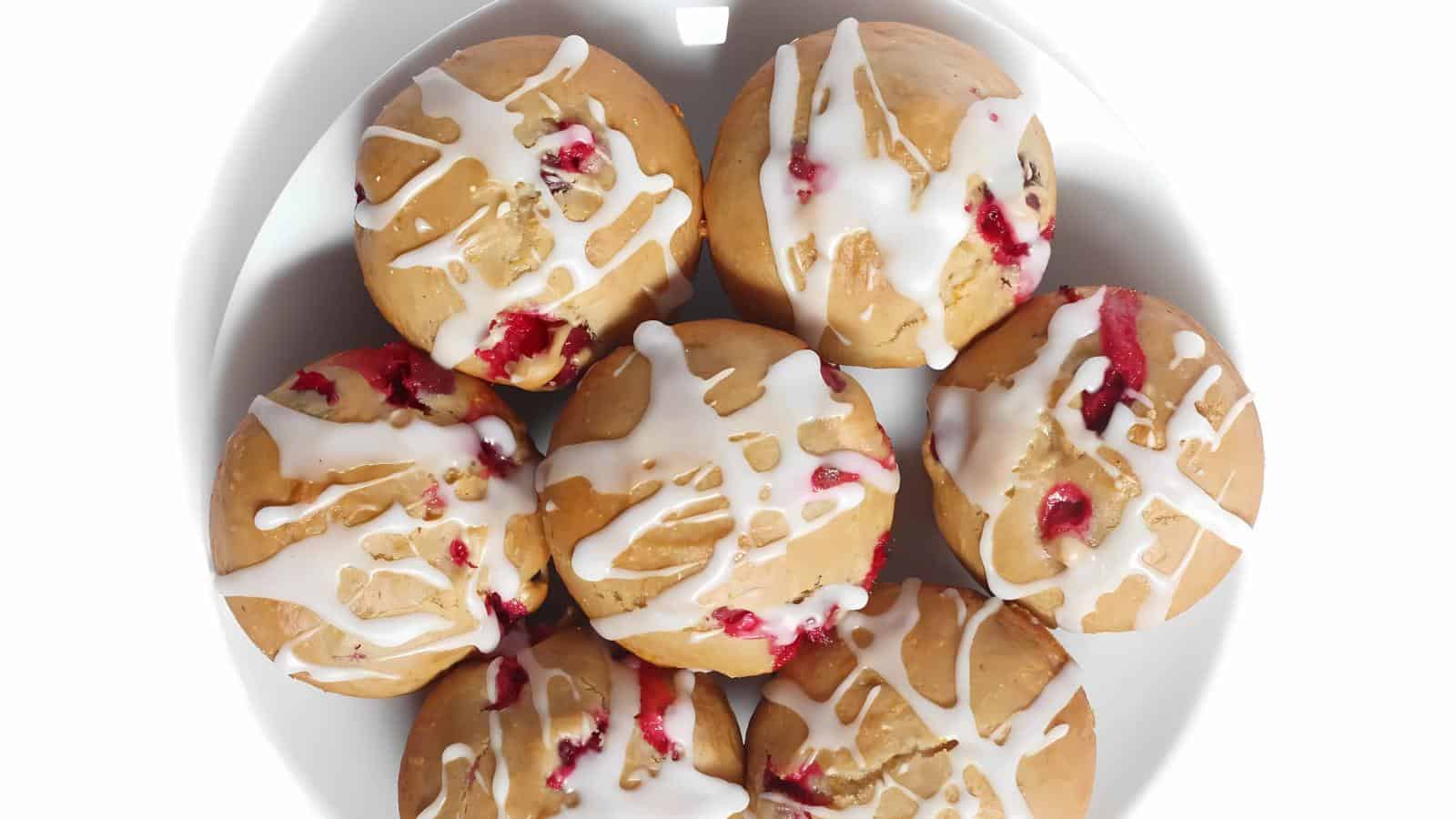A plate of seven muffins with red fruit bits and white icing drizzled on top.