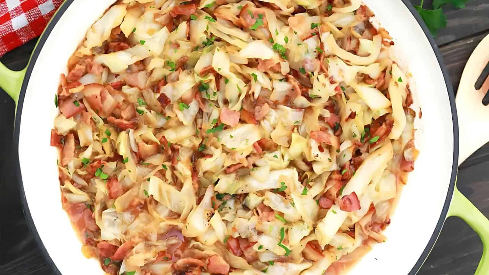 A close-up of fried cabbage with chopped bacon, garnished with herbs, displayed in a white dish.
