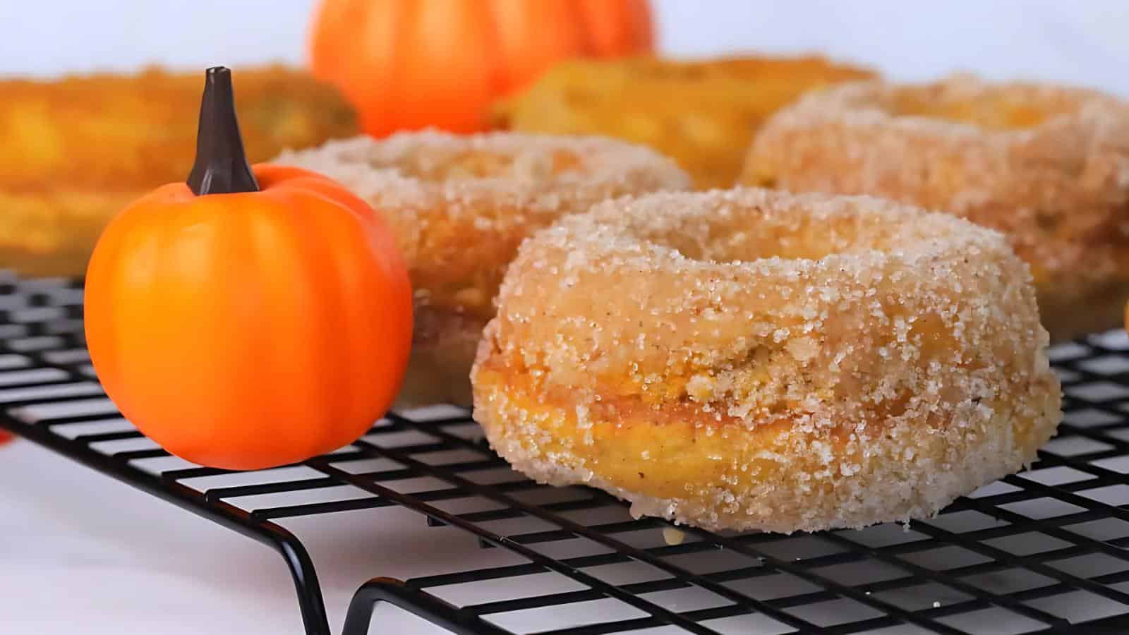 Sugar-coated donuts on a cooling rack with small decorative pumpkins in the background.