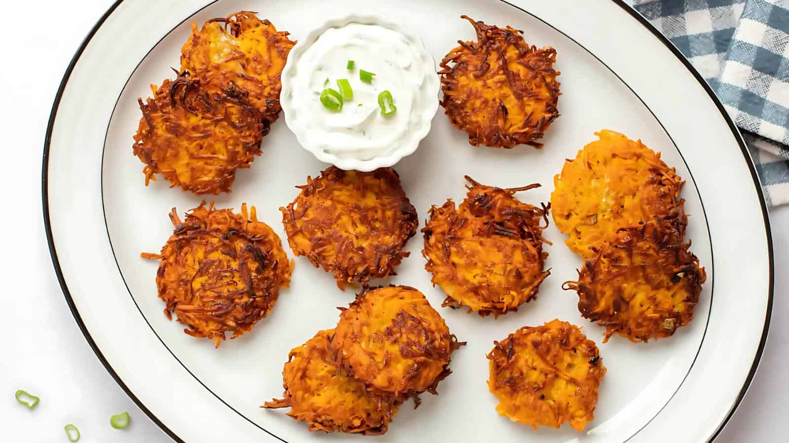 A plate of golden-brown hash brown patties arranged around a dish of sour cream topped with green onions.