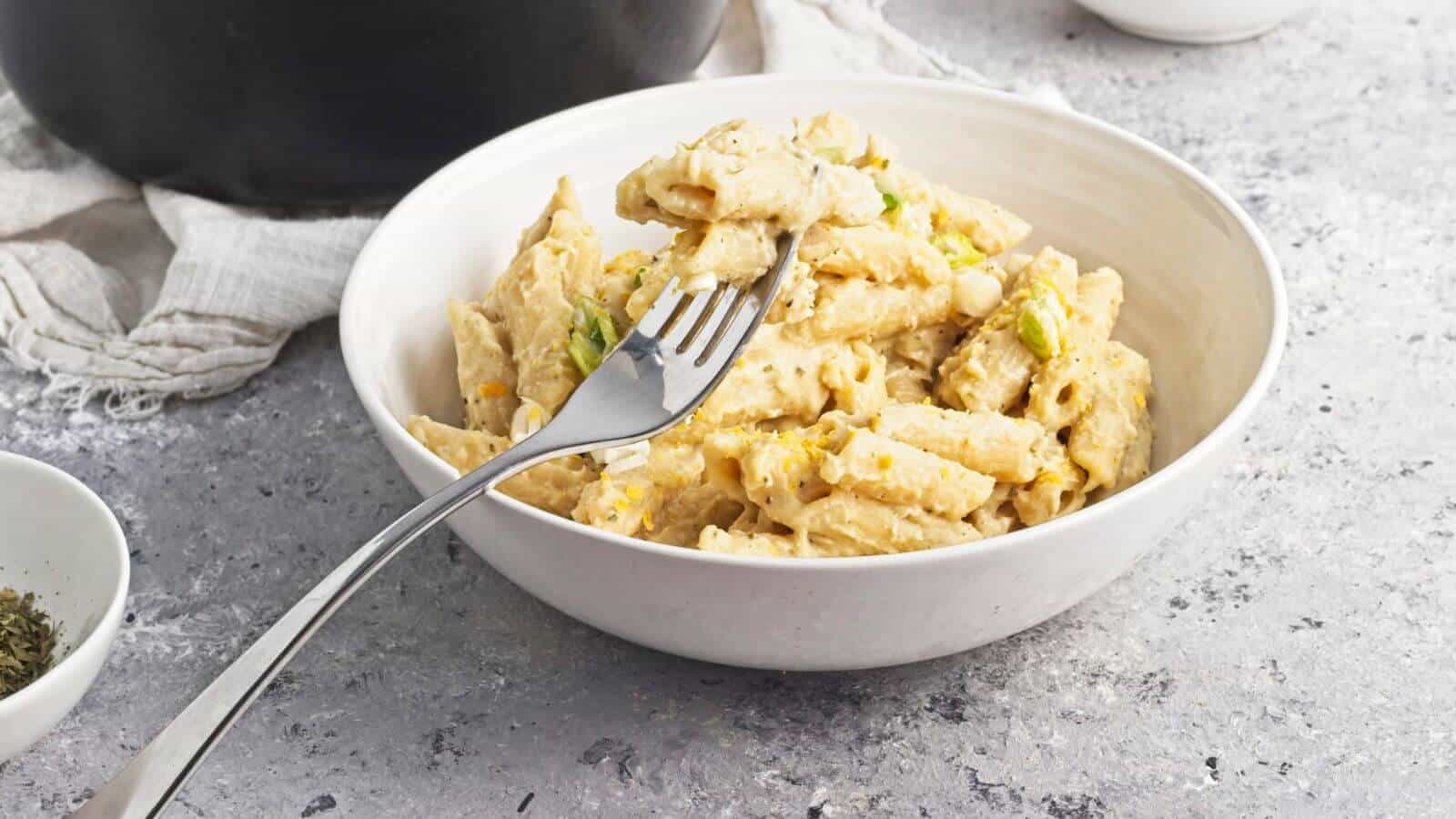 A bowl of creamy penne pasta with a fork, placed on a textured surface.