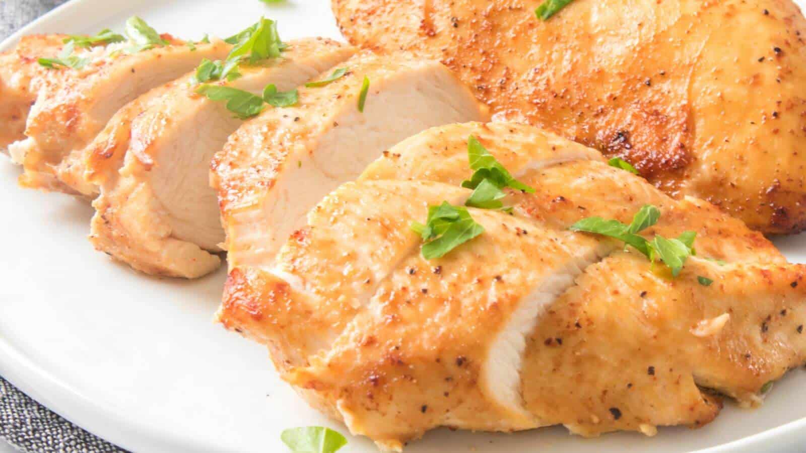 Sliced grilled chicken breast garnished with parsley on a white plate.