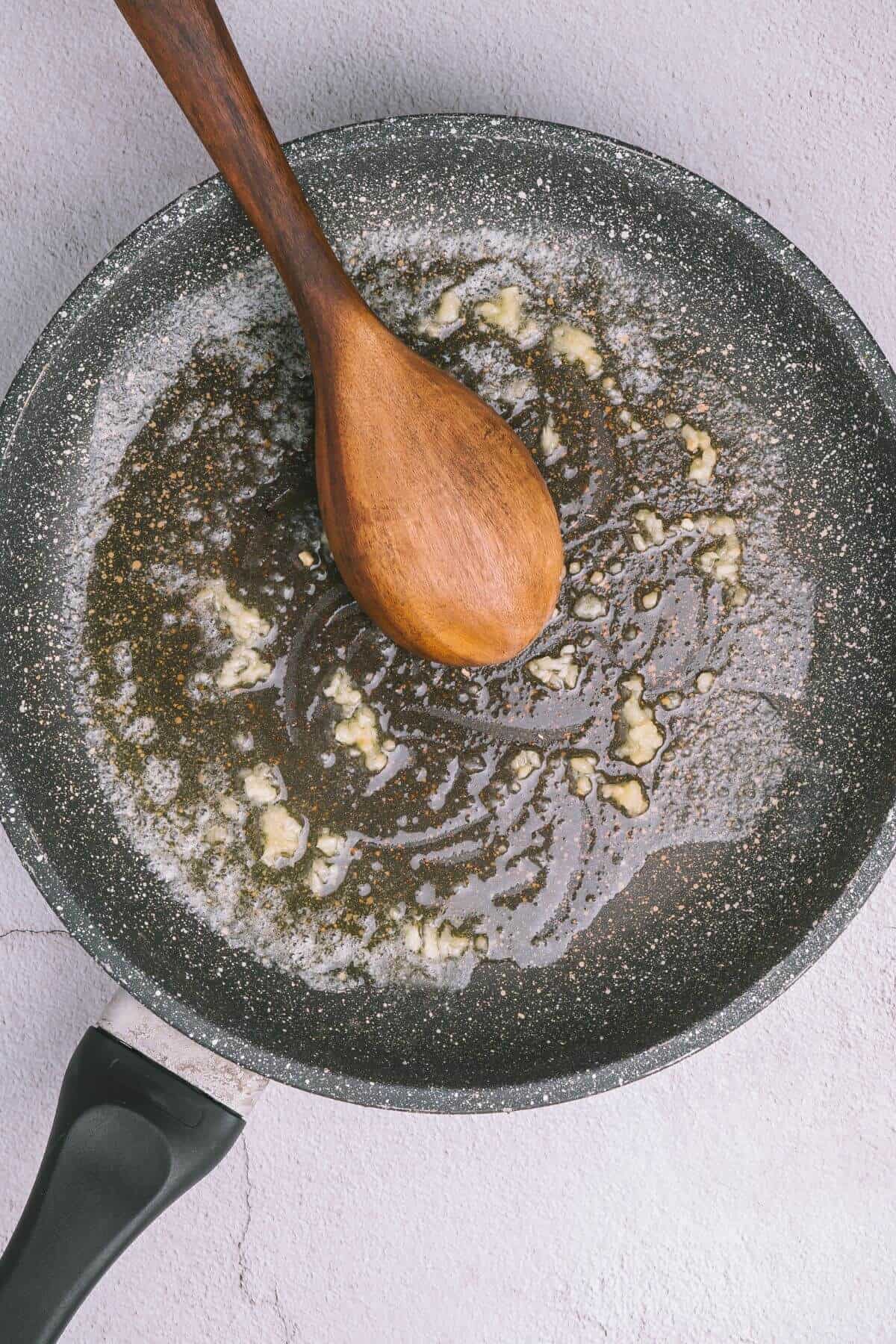 A wooden spoon in a frying pan melting butter and minced garlic.