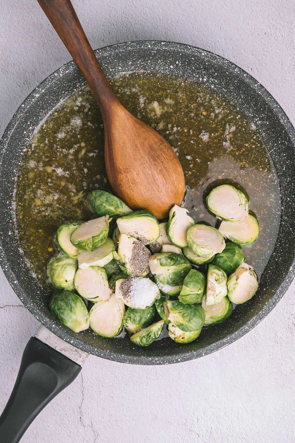 Brussels sprouts, butter, and spices in a frying pan with a wooden spoon on a light background.
