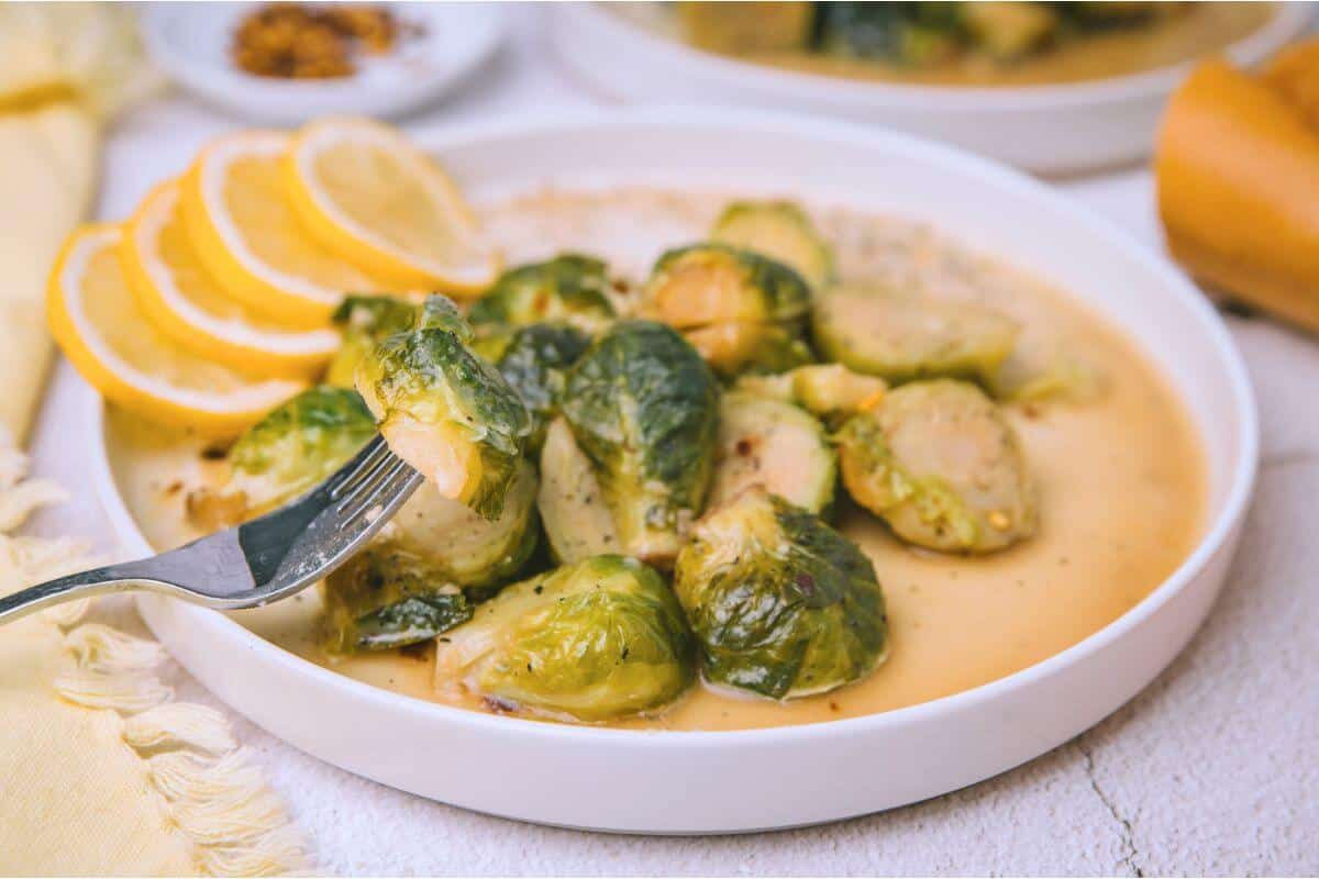 A plate of Brussels sprouts in sauce with a fork. Lemon slices are on the side.