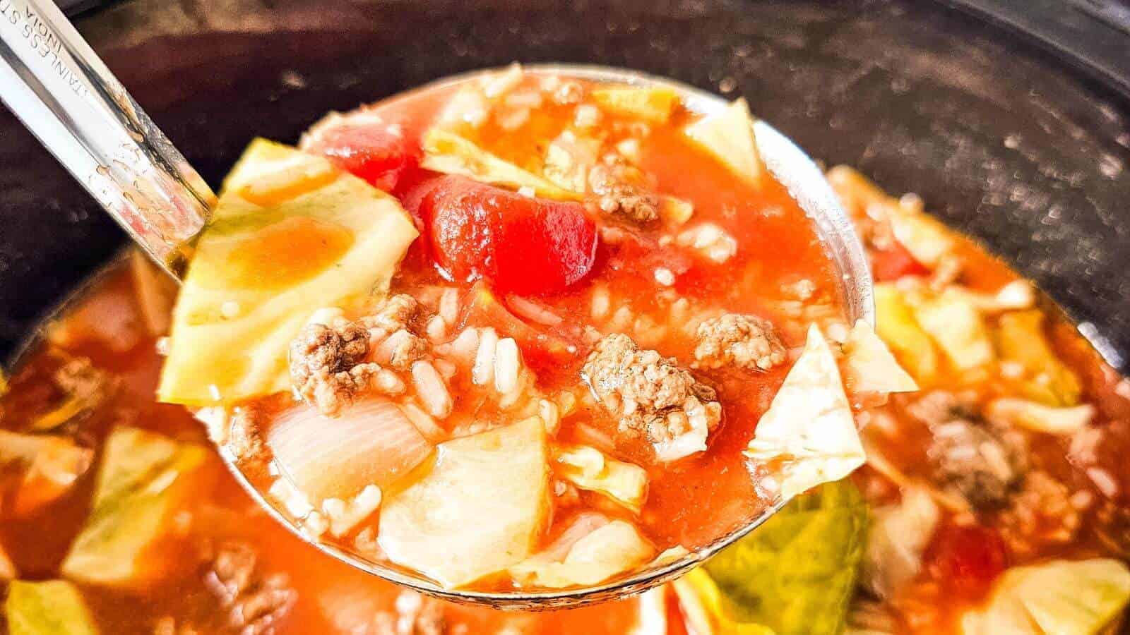 A ladle of soup with cabbage, ground meat, tomato pieces, and rice in a broth.