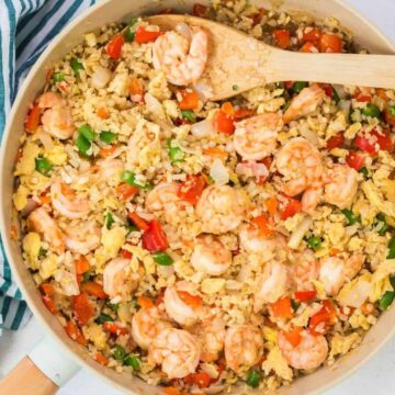 A skillet with shrimp fried rice mixed with vegetables and scrambled eggs, next to a striped cloth.