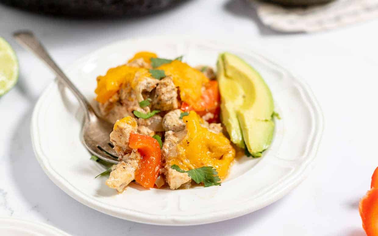A plate featuring cooked chicken, red bell peppers, cheese, and a slice of avocado, all beautifully garnished with cilantro. These casseroles taste like a chef made them, but you did! A fork rests invitingly on the side.