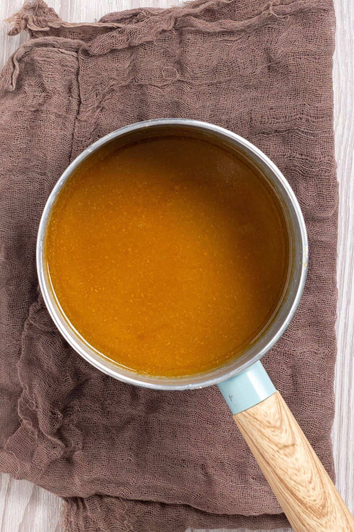 A saucepan filled with brown liquid on a brown cloth.