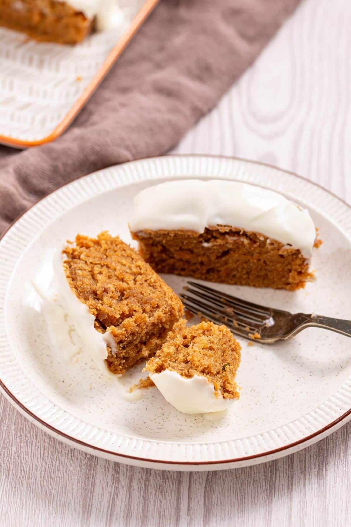 A slice of carrot cake with white frosting on a plate, partially eaten, with a fork beside it.