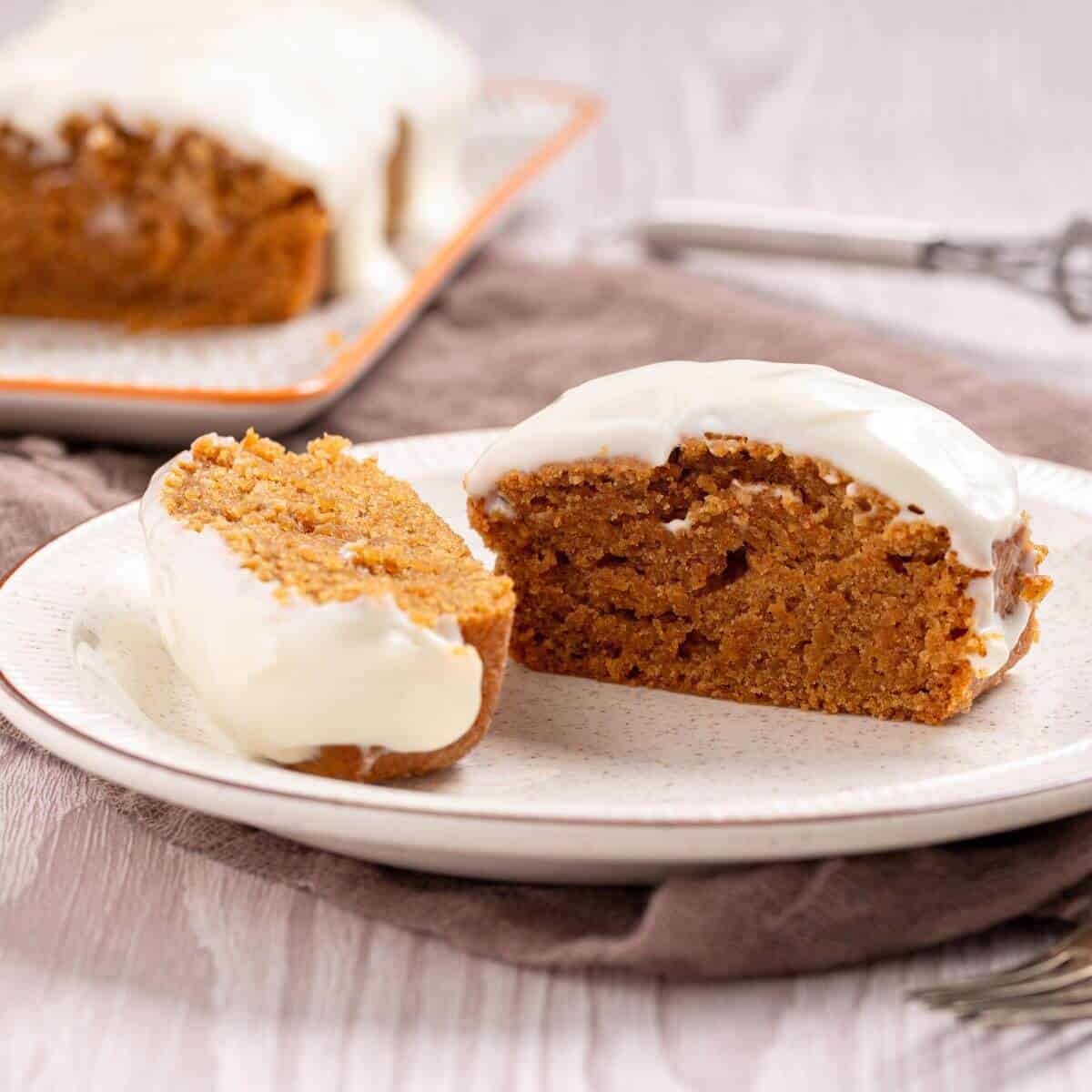Sliced pumpkin cake with white icing on a white plate, set on a wooden table.