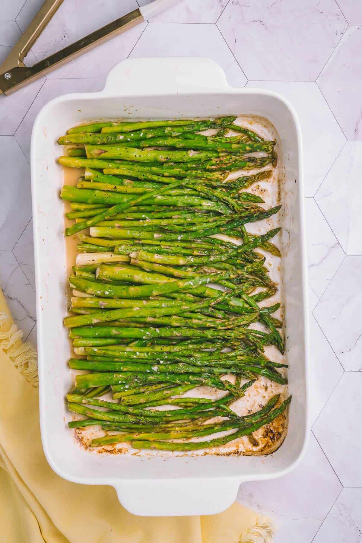 A baking dish filled with oven-roasted asparagus spears, lightly seasoned with spices.