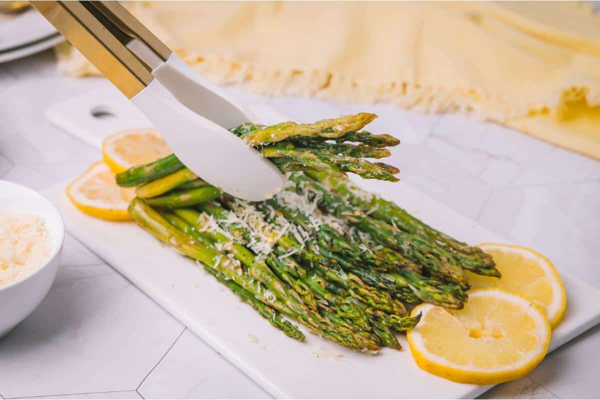 A serving of roasted asparagus topped with grated cheese and lemon slices on a white platter.