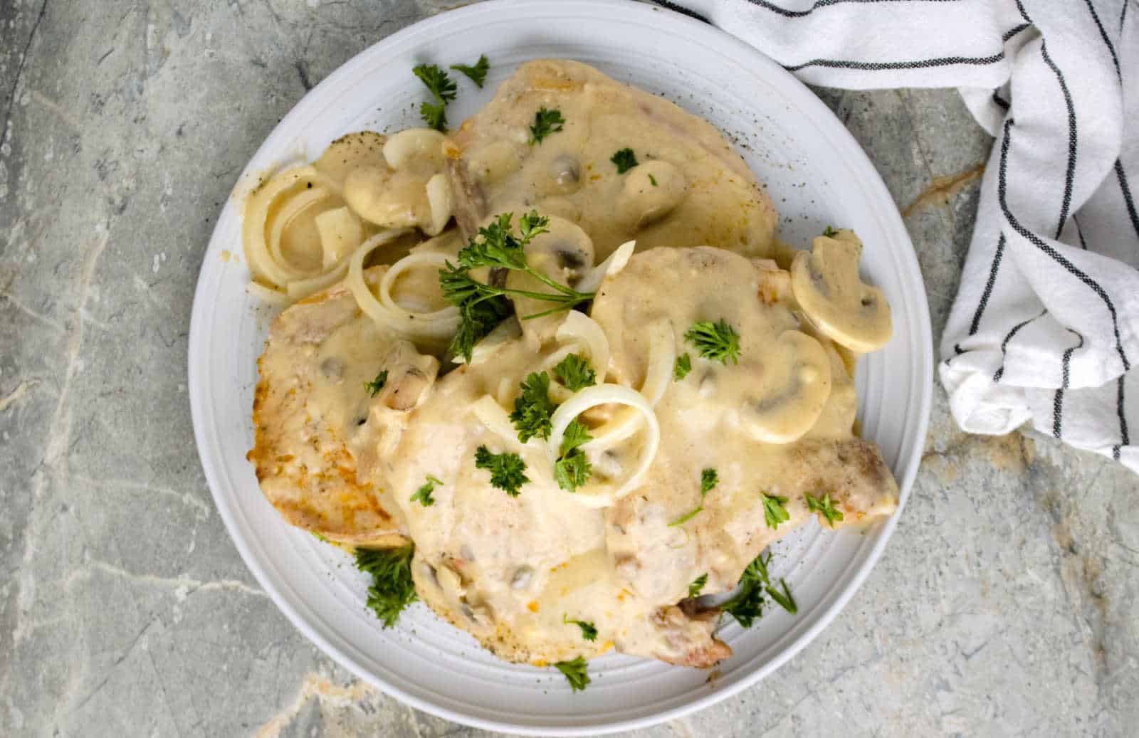 A plate of pork chops covered in creamy mushroom sauce, garnished with parsley and onion slices.