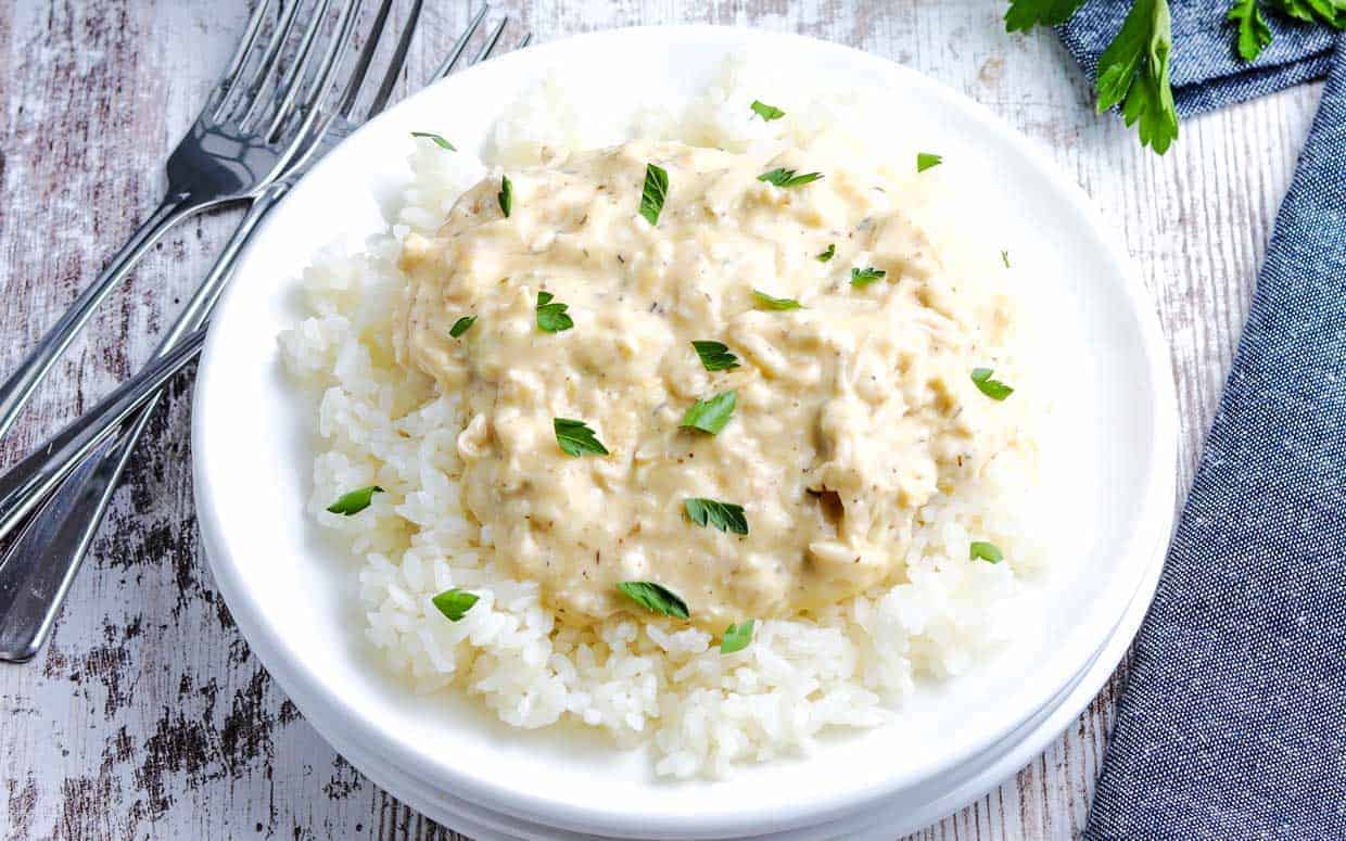 A plate of white rice topped with creamy chicken gravy, garnished with green herbs. Forks are placed beside the dish on a wooden surface.