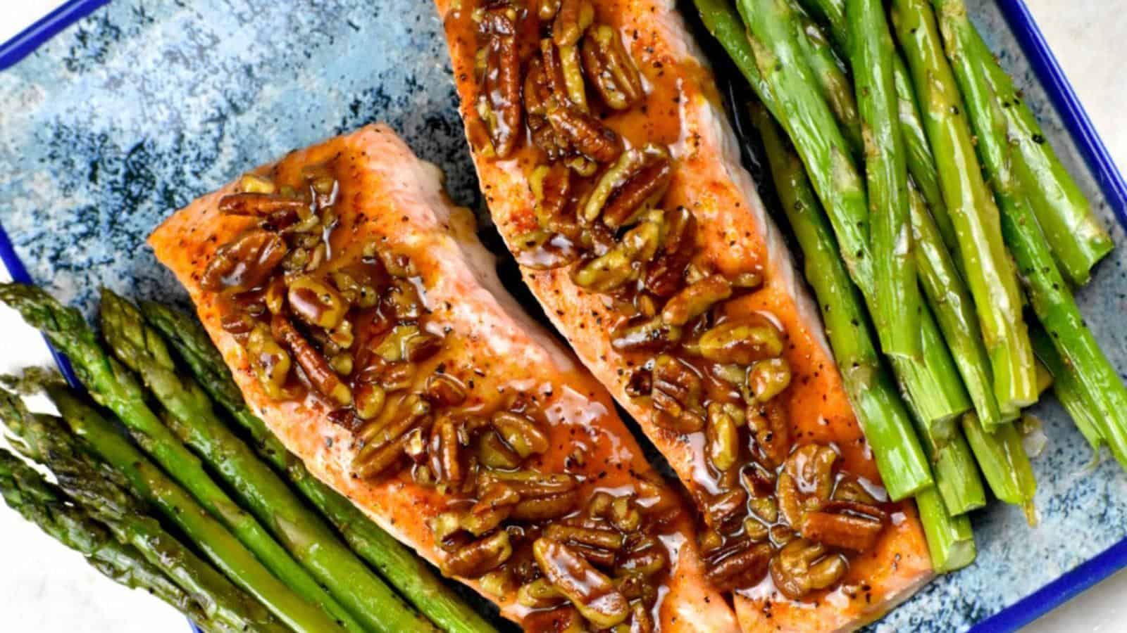 Two grilled salmon fillets topped with chopped pecans, served with a side of asparagus on a blue plate.