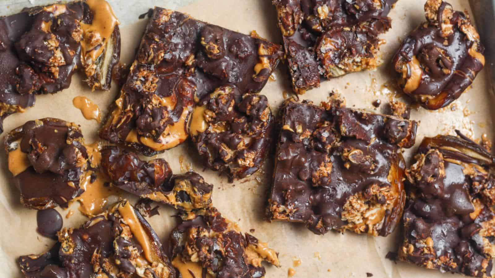 A batch of chocolate and peanut butter bars on parchment paper, some whole and some broken into pieces.