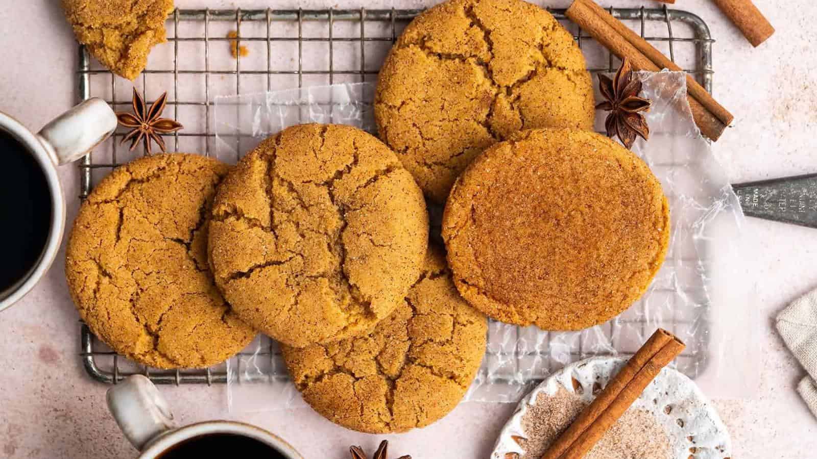 Gingersnap cookies on a cooling rack, surrounded by cinnamon sticks and star anise, with two cups of black coffee nearby.
