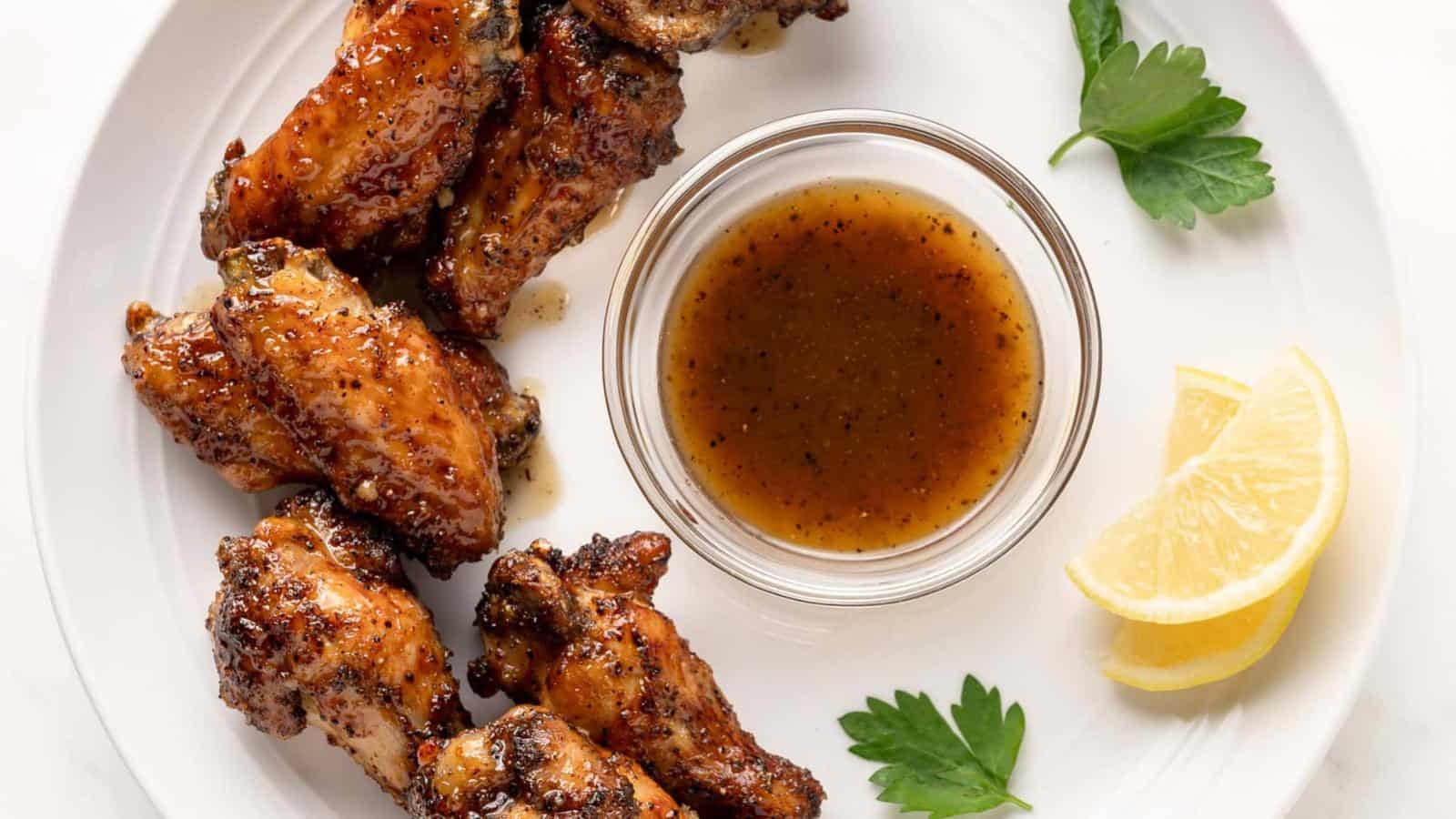 Plate of glazed chicken wings with a small bowl of sauce, lemon wedges, and parsley garnishes.