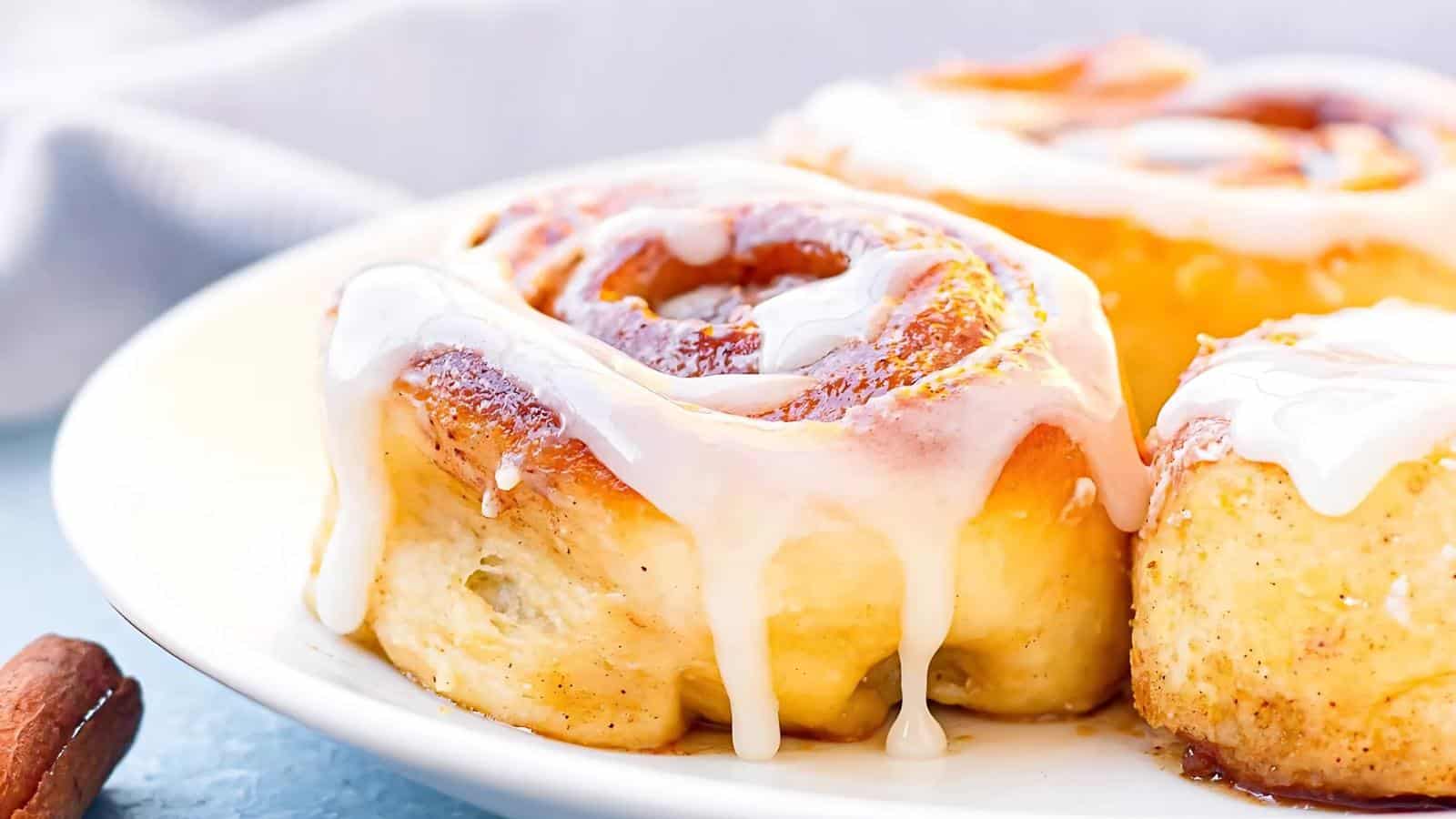 Close-up of frosted cinnamon rolls on a white plate.