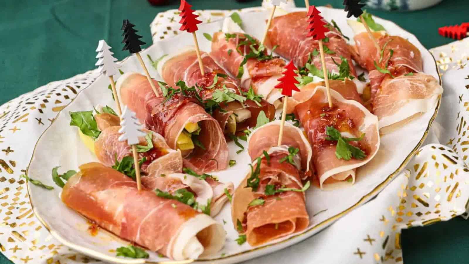 A plate of prosciutto-wrapped appetizers garnished with herbs and skewered with decorative picks shaped like small trees.