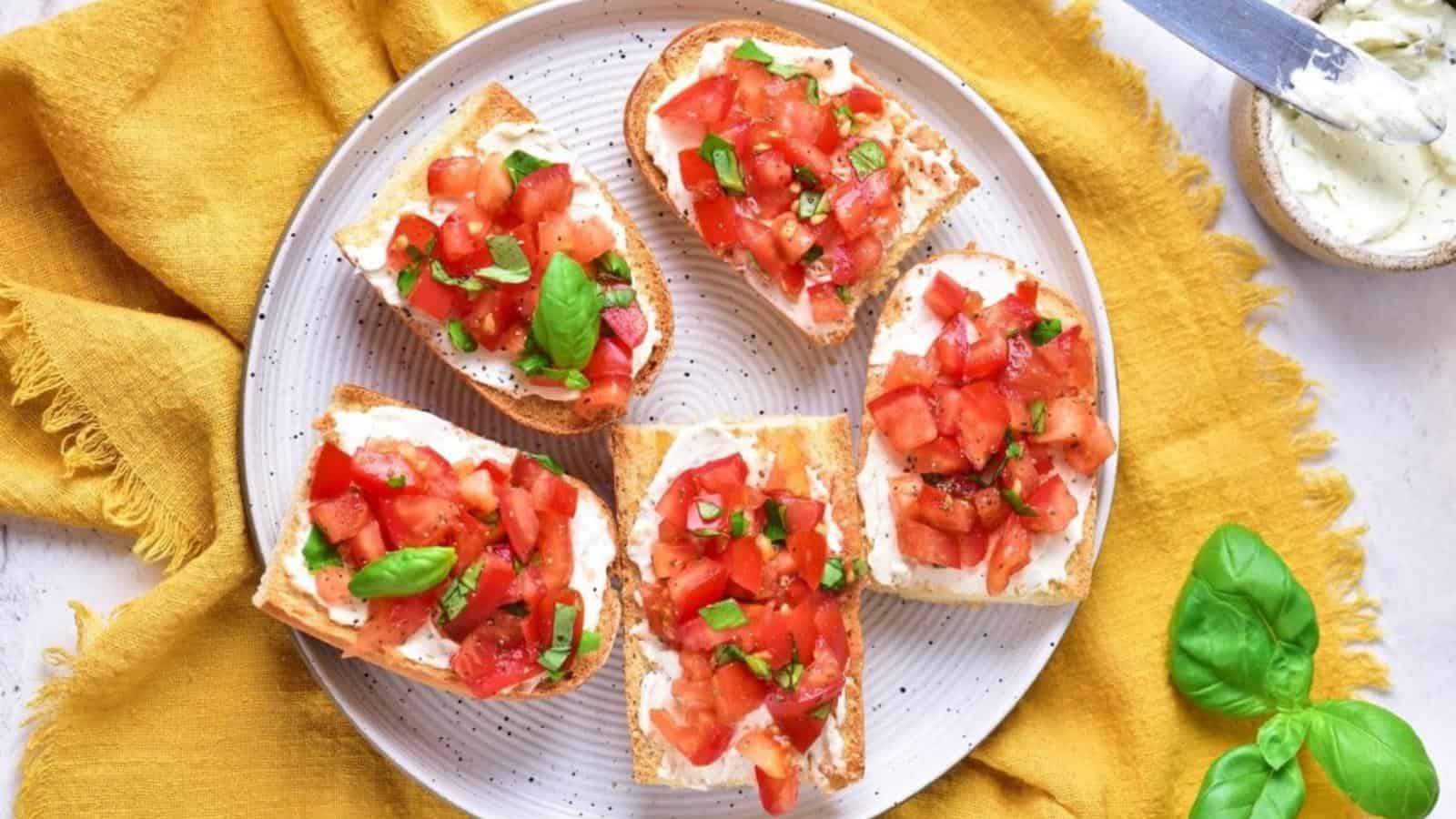Plate of bruschetta with diced tomatoes and basil on toasted bread, set on a yellow cloth.