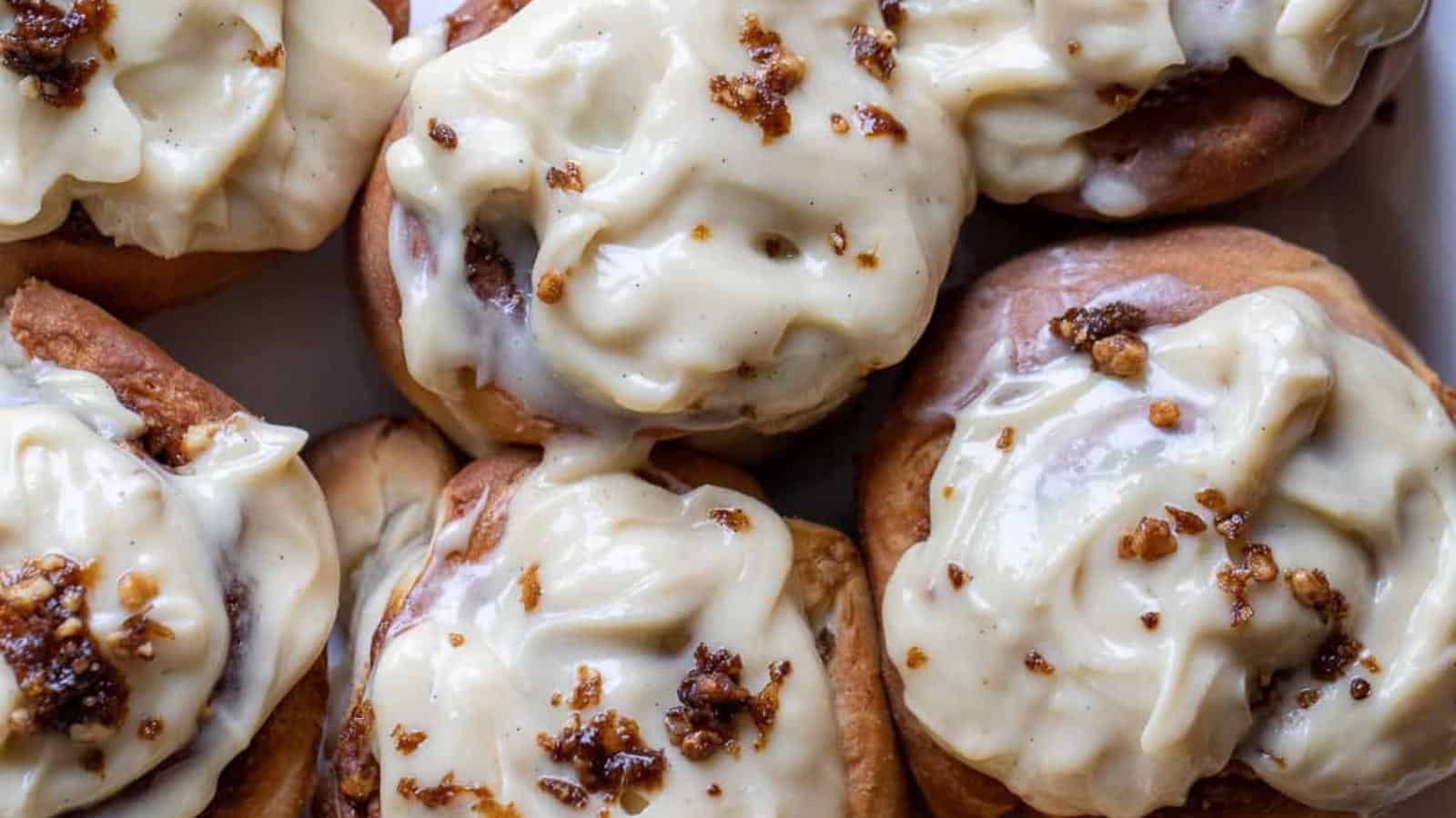 Close-up of six cinnamon rolls topped with creamy icing and sprinkled with nuts.