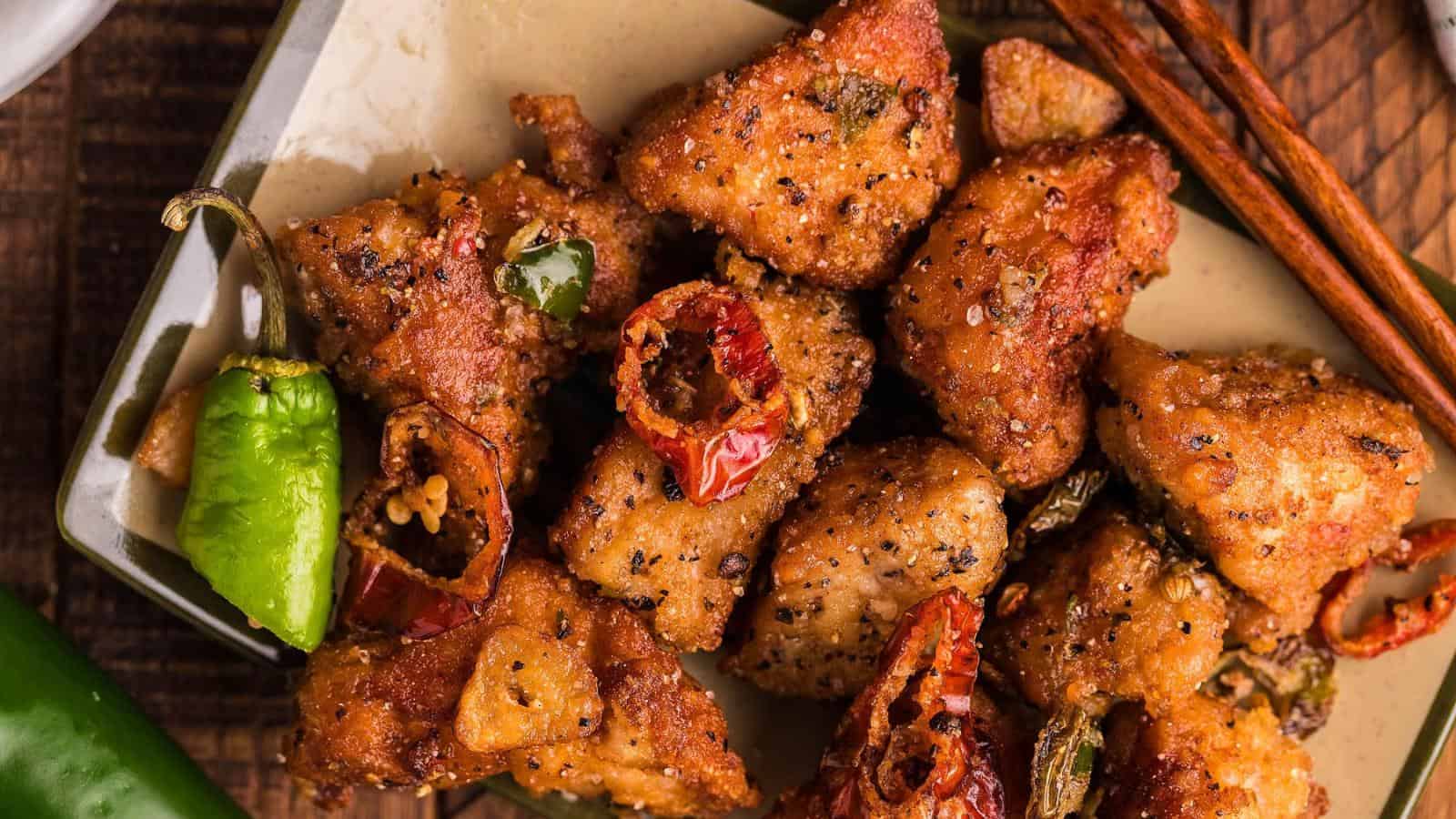A plate of crispy fried chicken pieces seasoned with black pepper and garnished with green and red chili peppers.