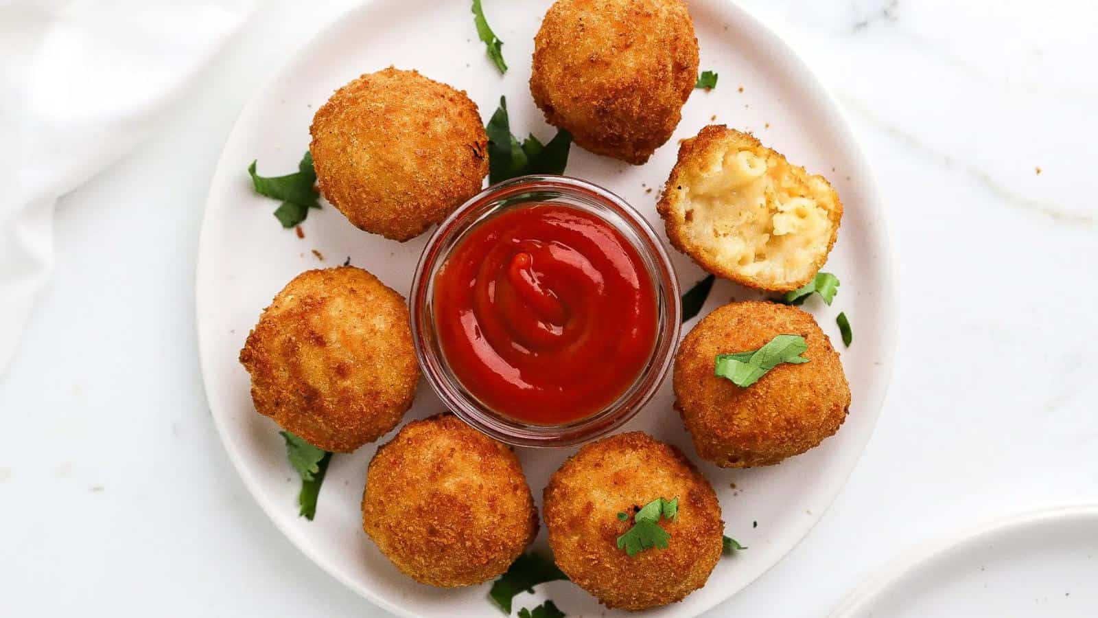 Plate of fried arancini balls arranged around a small bowl of tomato sauce, garnished with parsley. One arancini is cut open showing a creamy interior.