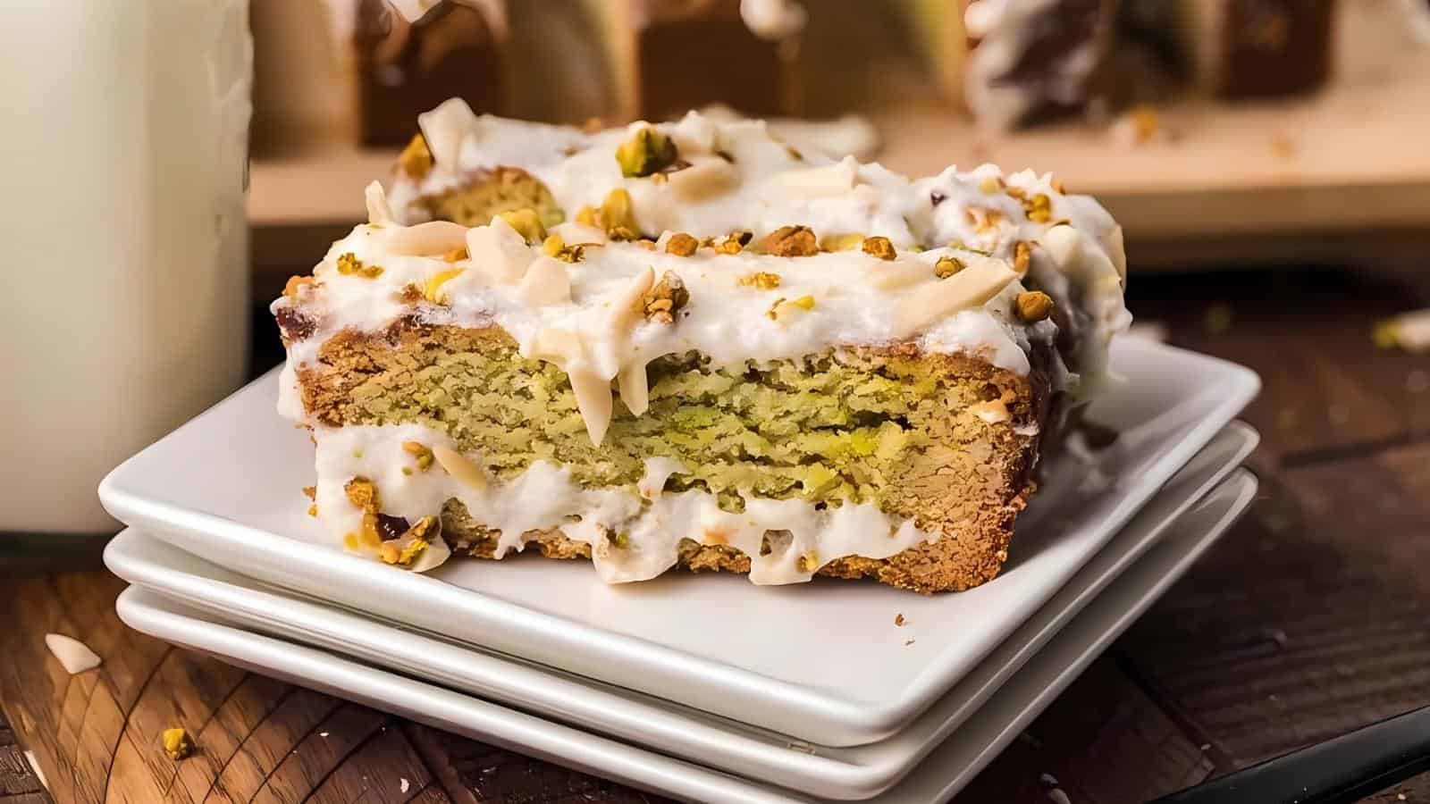A slice of frosted pistachio cake with chopped nuts on top, served on stacked white plates.