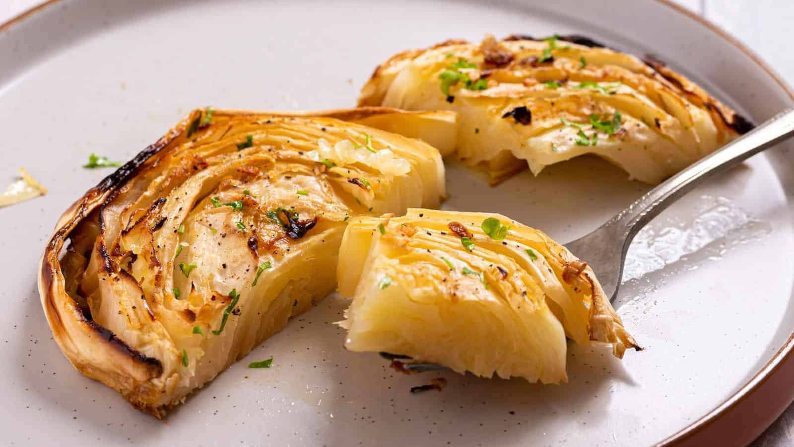 Grilled cabbage wedge on a plate, partially cut, with a fork and sprinkled with herbs.