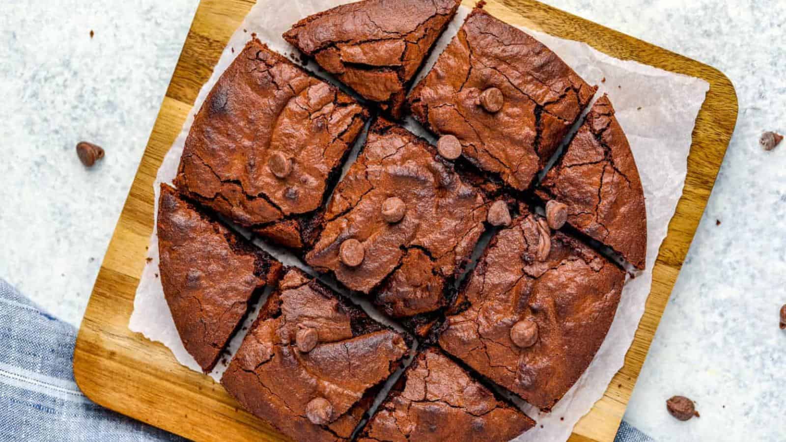A round chocolate brownie, cut into eight pieces, on a wooden board with parchment paper.