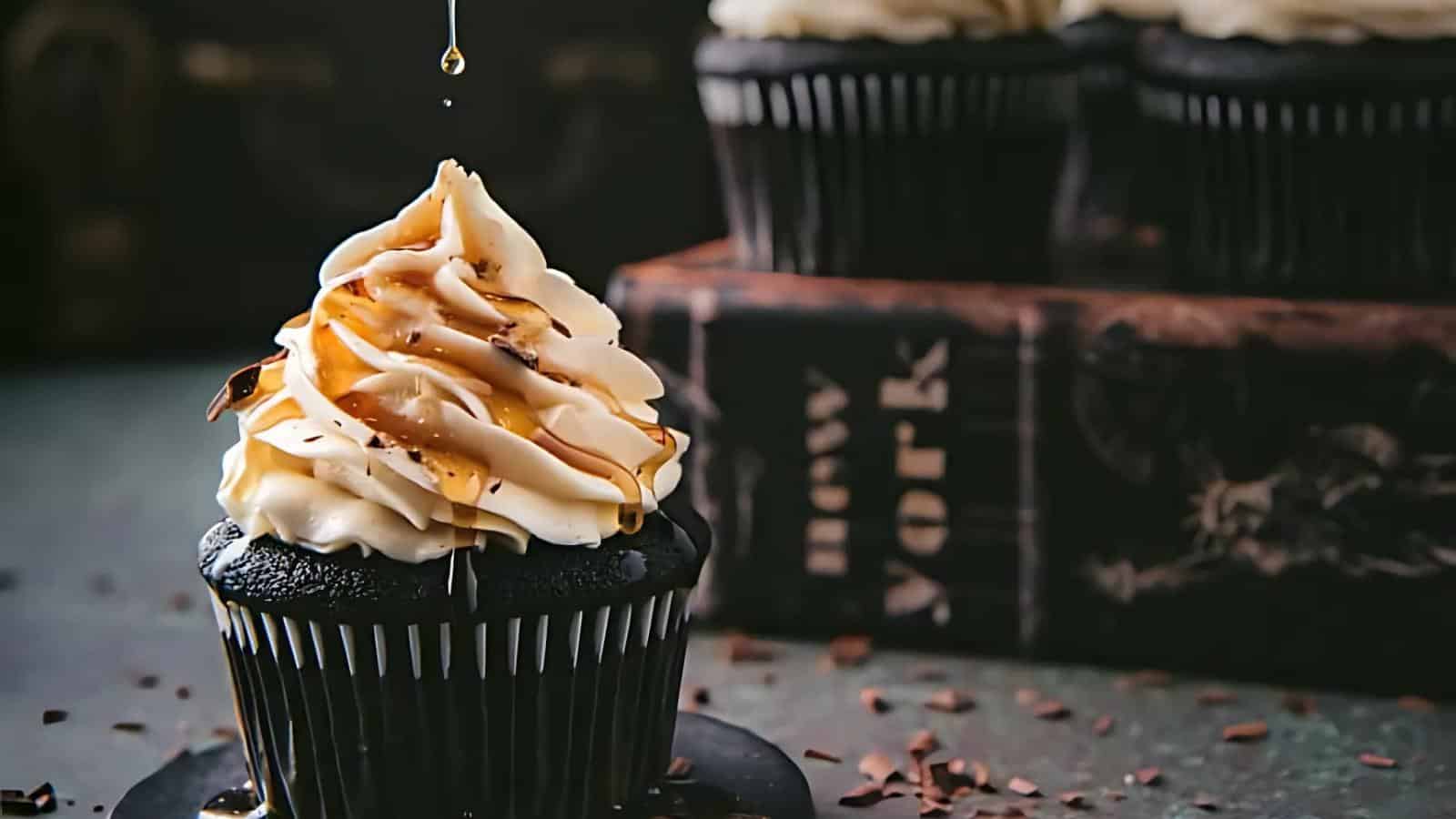 A chocolate cupcake with swirled frosting is drizzled with caramel. Books labeled "New York" are in the background.