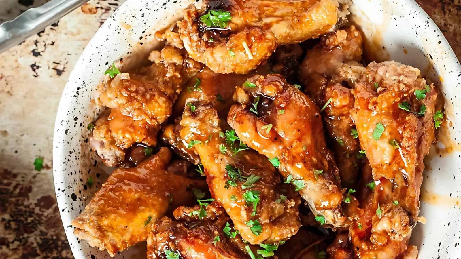 A bowl of glazed chicken wings garnished with chopped herbs.