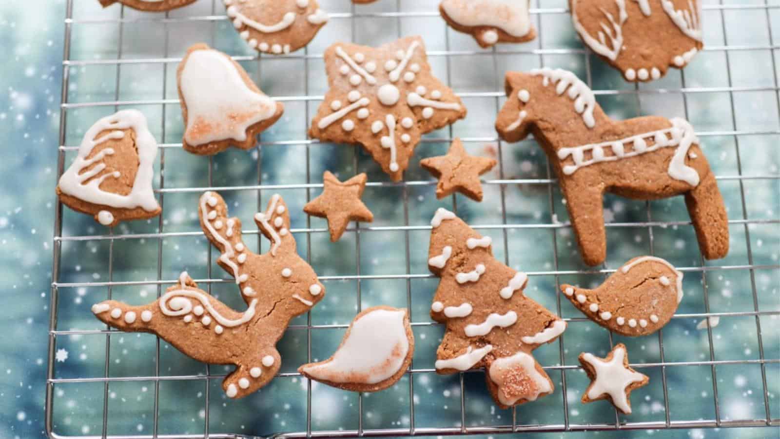 Christmas-themed gingerbread cookies with white icing, featuring stars, trees, animals, and bells, arranged on a cooling rack.