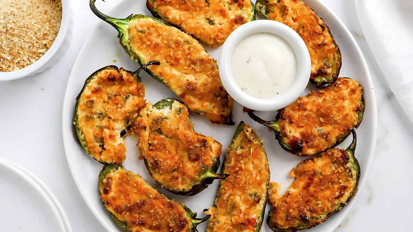 Plate of baked jalapeño poppers with a small bowl of dipping sauce in the center.