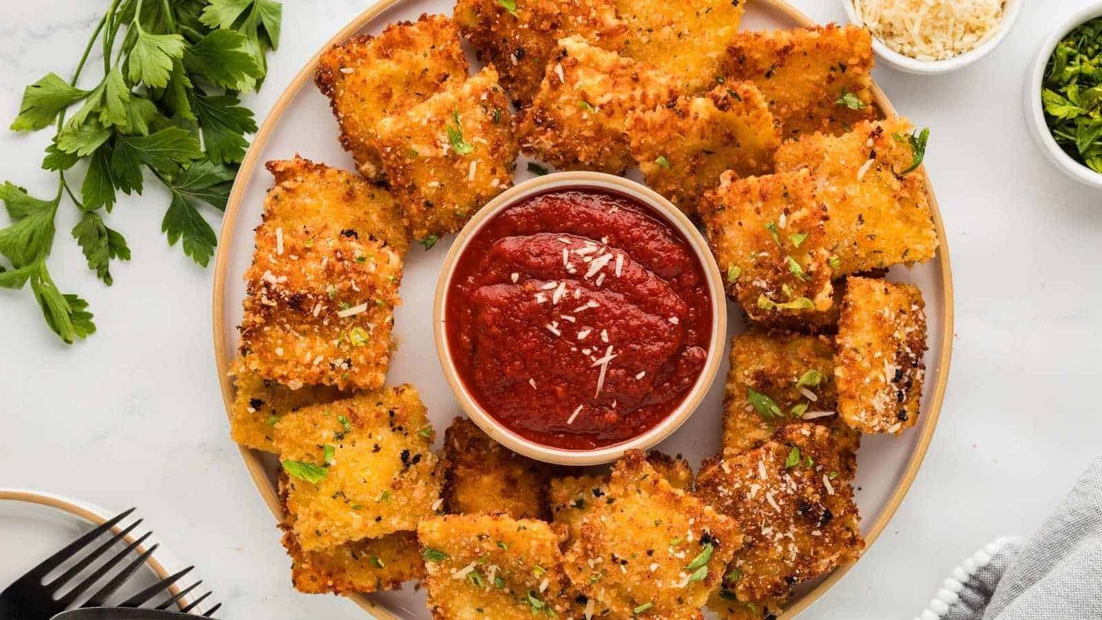 A plate of crispy breaded ravioli is arranged in a circle around a bowl of marinara sauce, garnished with parsley and parmesan cheese.