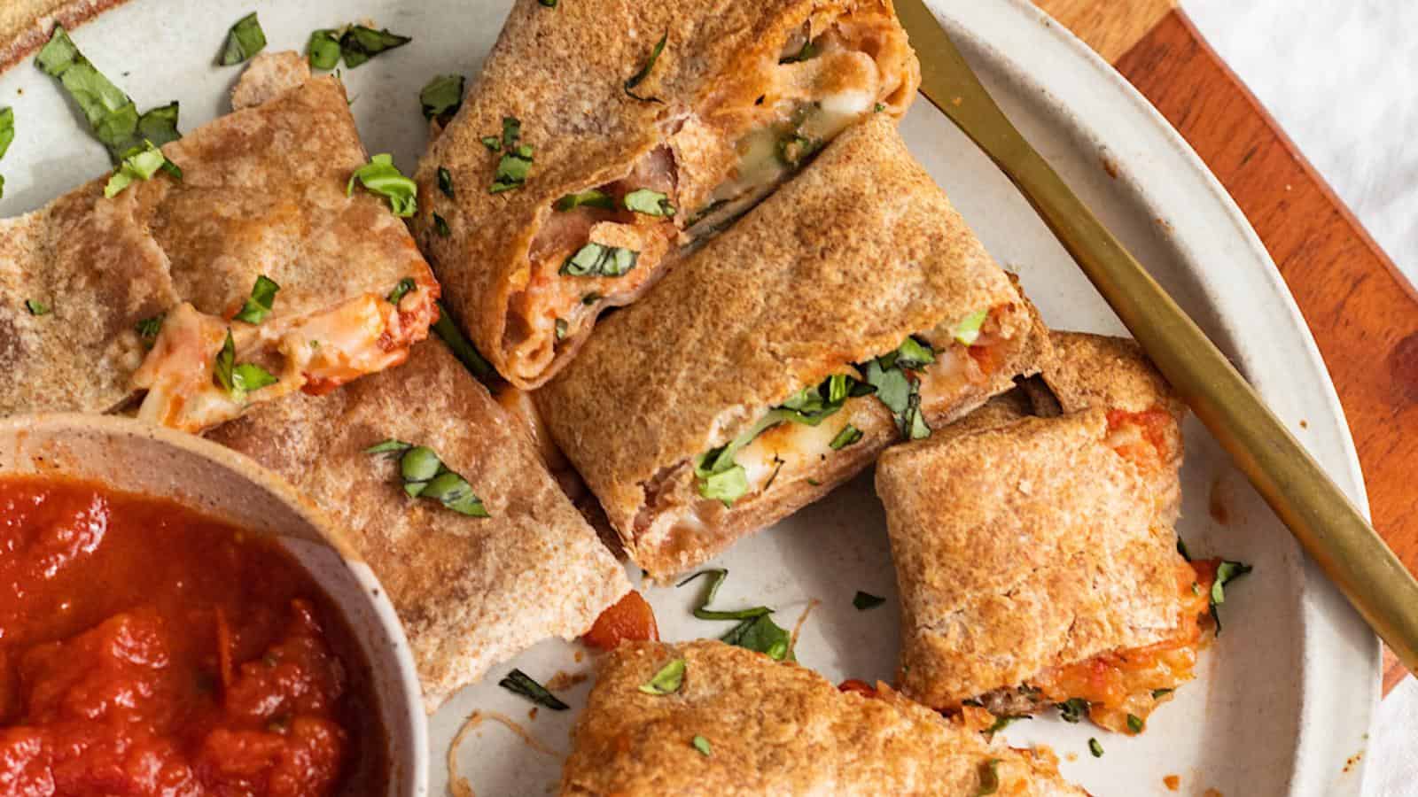 A plate of cheesy pizza rolls with a side of marinara sauce, garnished with chopped herbs.