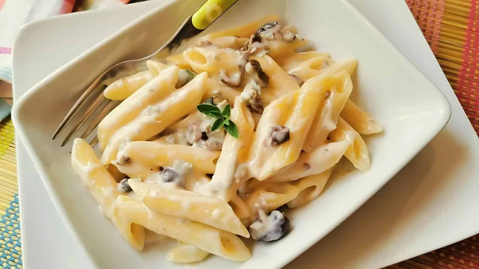 Penne pasta in a creamy white sauce with mushrooms, garnished with fresh herbs, served on a white plate with a fork.