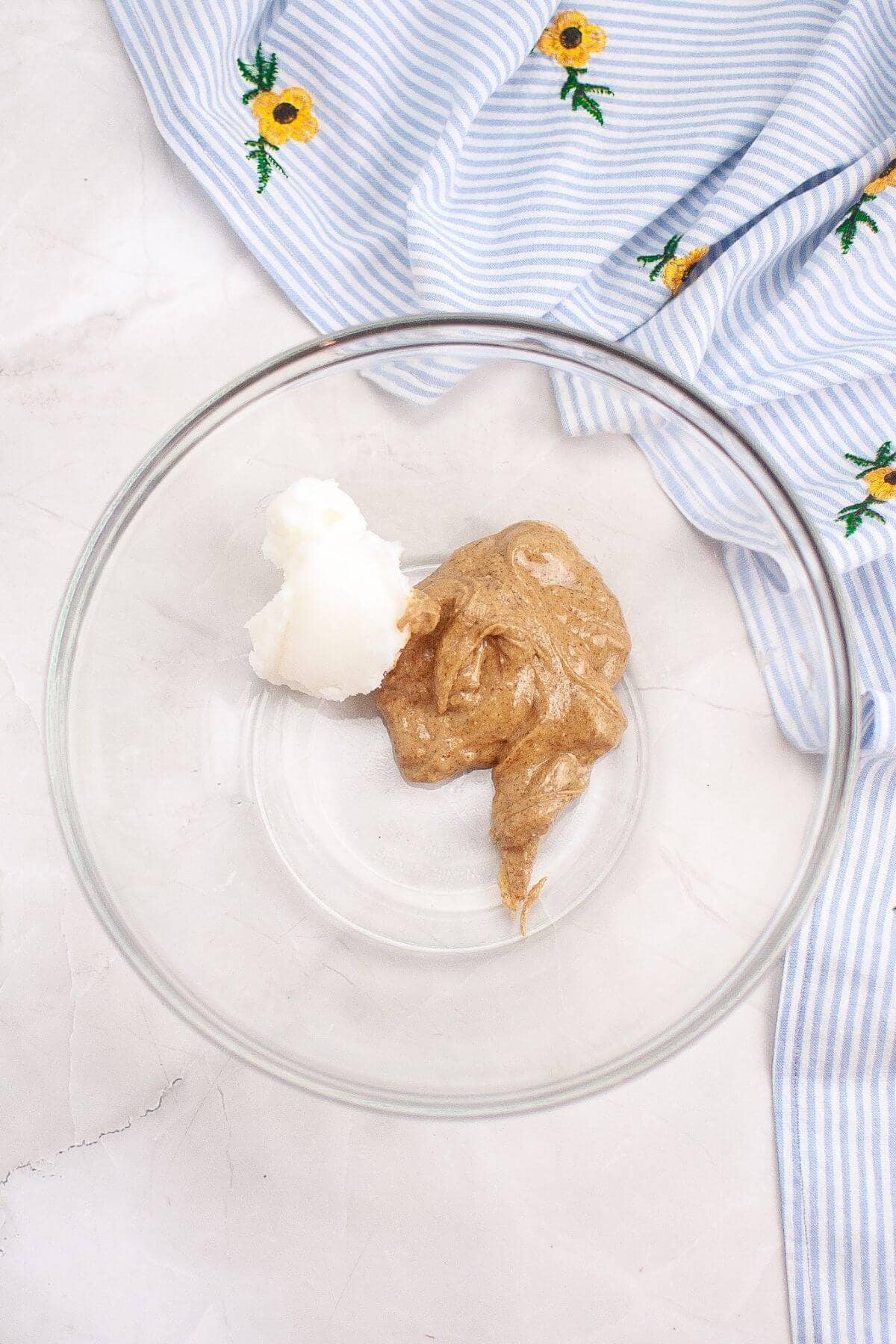 A glass bowl with blobs of brown and white paste. A striped cloth with floral embroidery is beside the bowl.