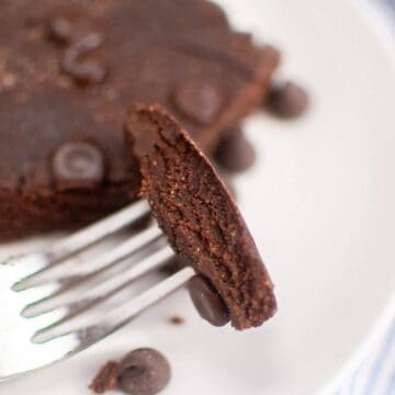 Fork holding a slice of a chocolate brownie with chocolate chips on a white plate.