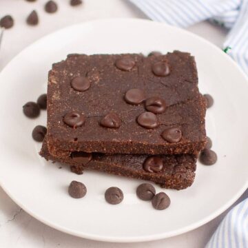 Two stacked chocolate brownies on a white plate, topped with chocolate chips, with extra chips scattered around.