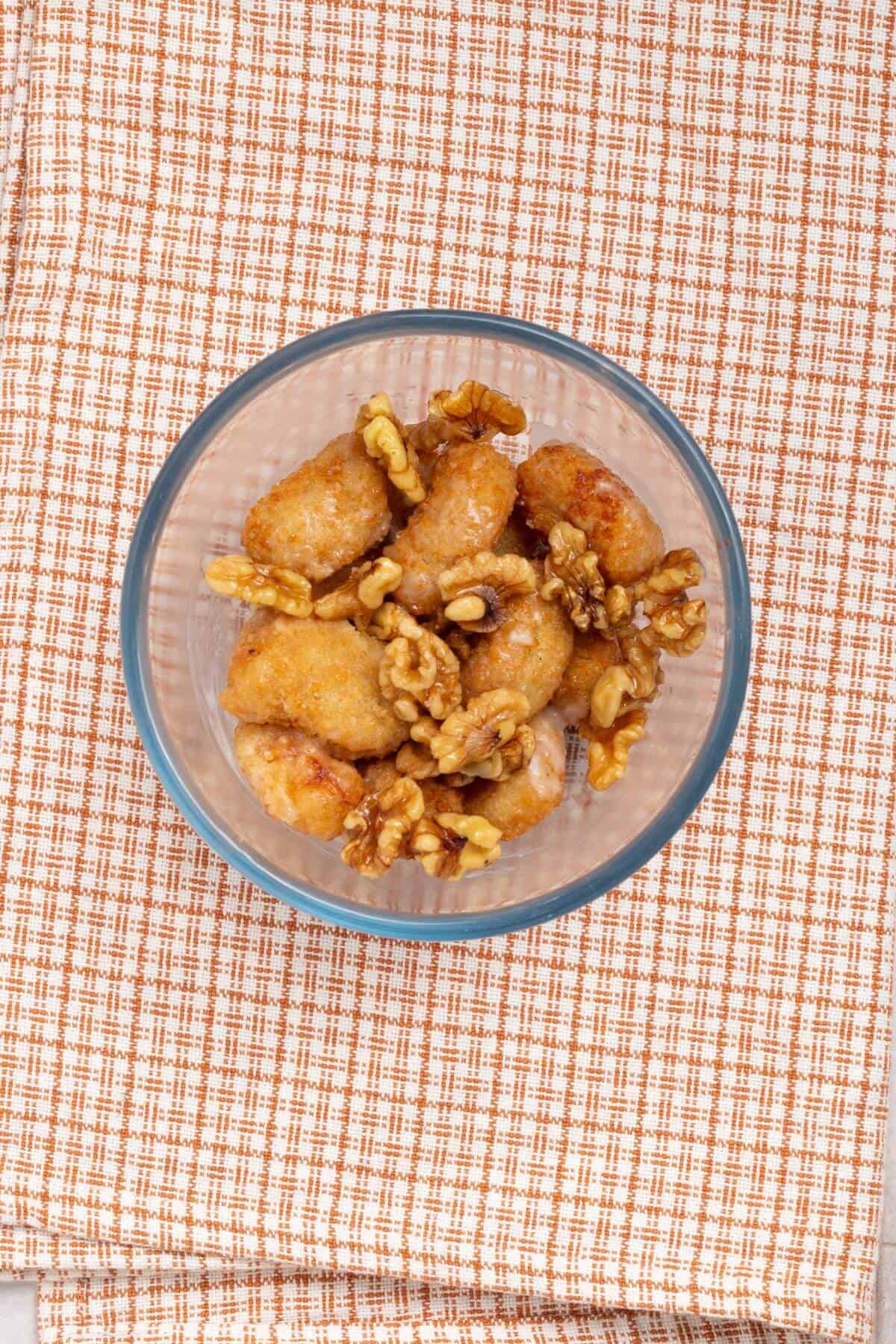 A bowl of bite-sized pastries topped with walnuts, placed on a checkered fabric.