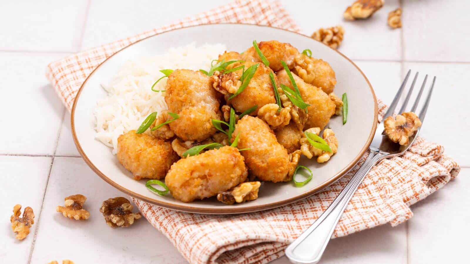 Plate of crispy tofu pieces with walnuts and green onions, served alongside white rice. Fork on the side.